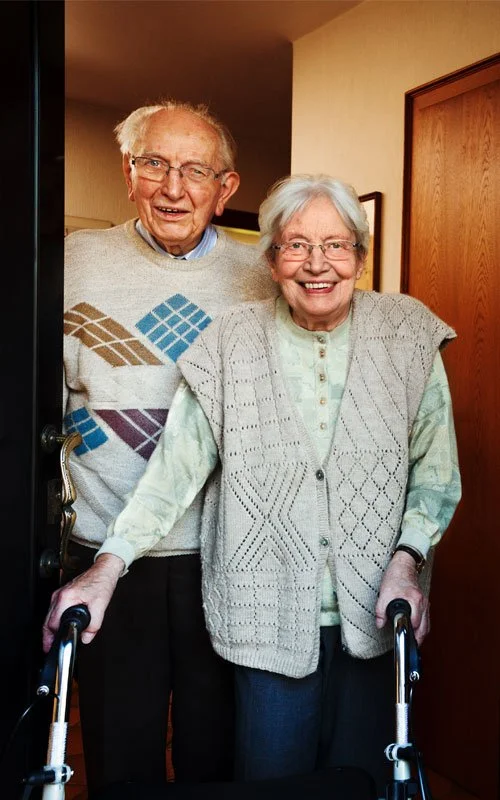 An elderly couple in a doorway, the lady using a walker