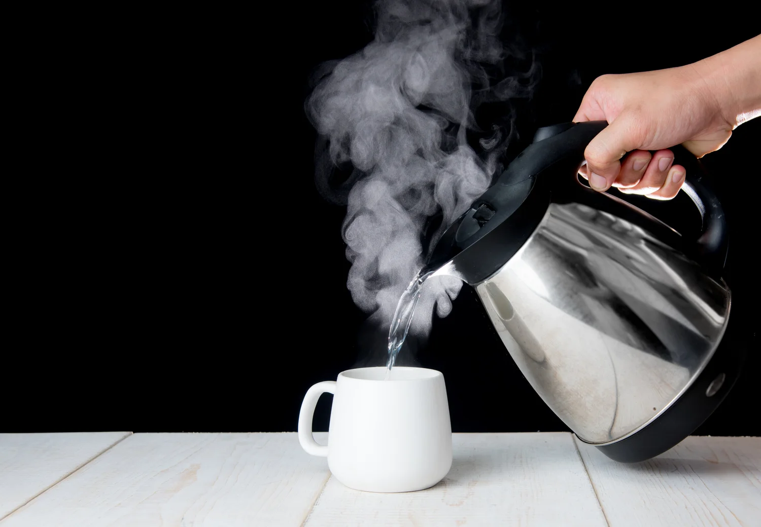 A hand pouring boiling water from a kettle into a mug